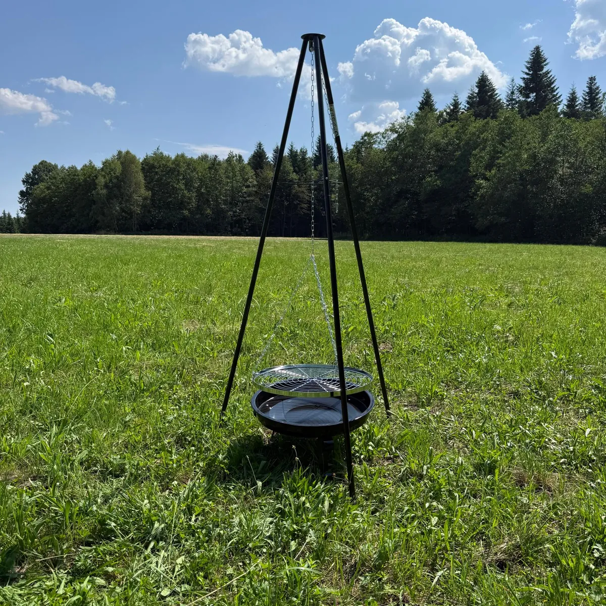 Stalowy trójnóg grillowy Hefajstos ustawiony na łące na tle lasu