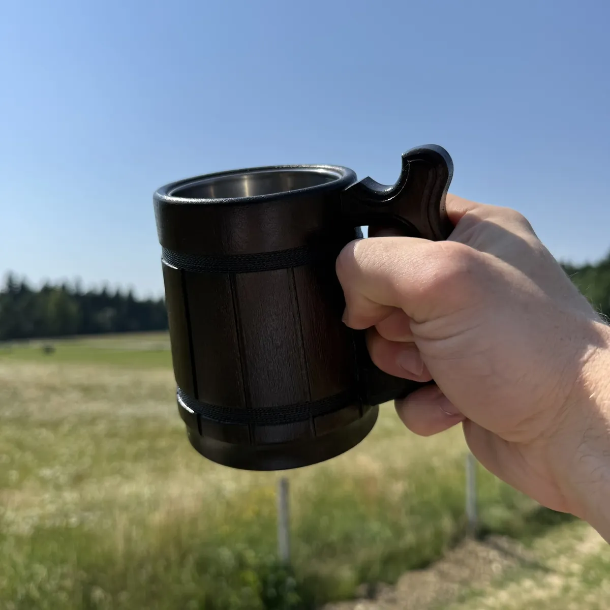 Dłoń trzymająca ciemny dębowy kufel 330 ml za rzeźbione ucho na tle łąki